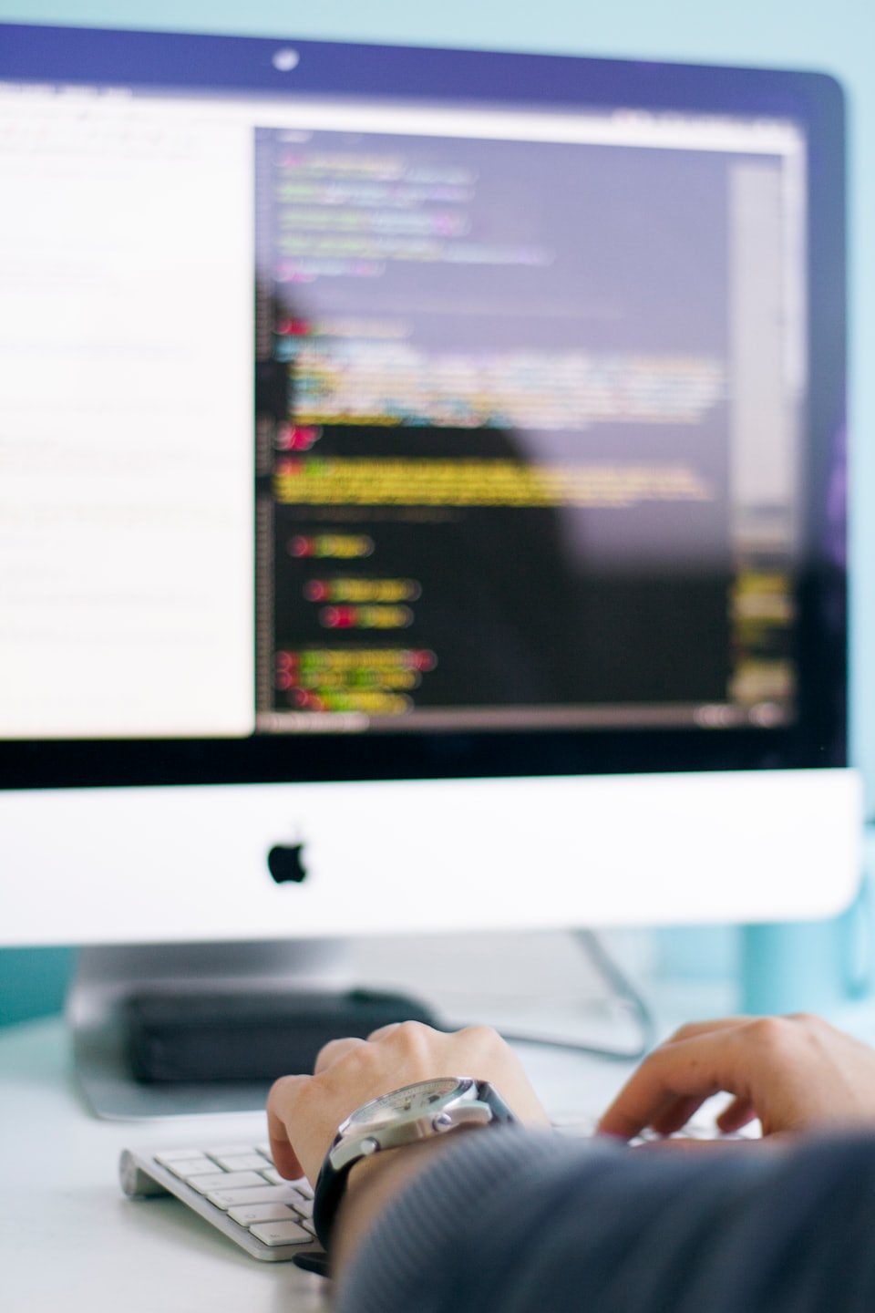 Hände tippen auf einer weißen Tastatur mit einem Monitor, der Code anzeigt.