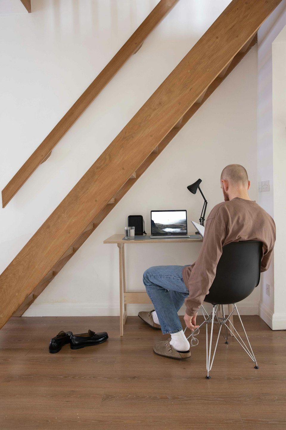 Mann arbeitet am Laptop am Schreibtisch unter der Treppe.