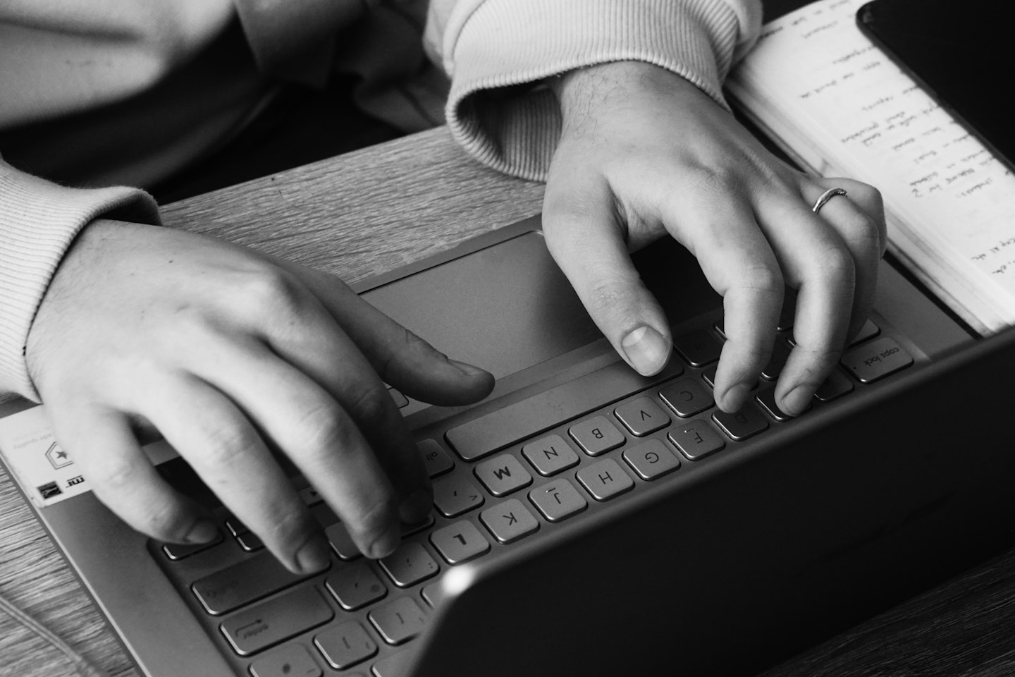 Hände tippen auf einer silbernen Laptop-Tastatur auf einem Holztisch.